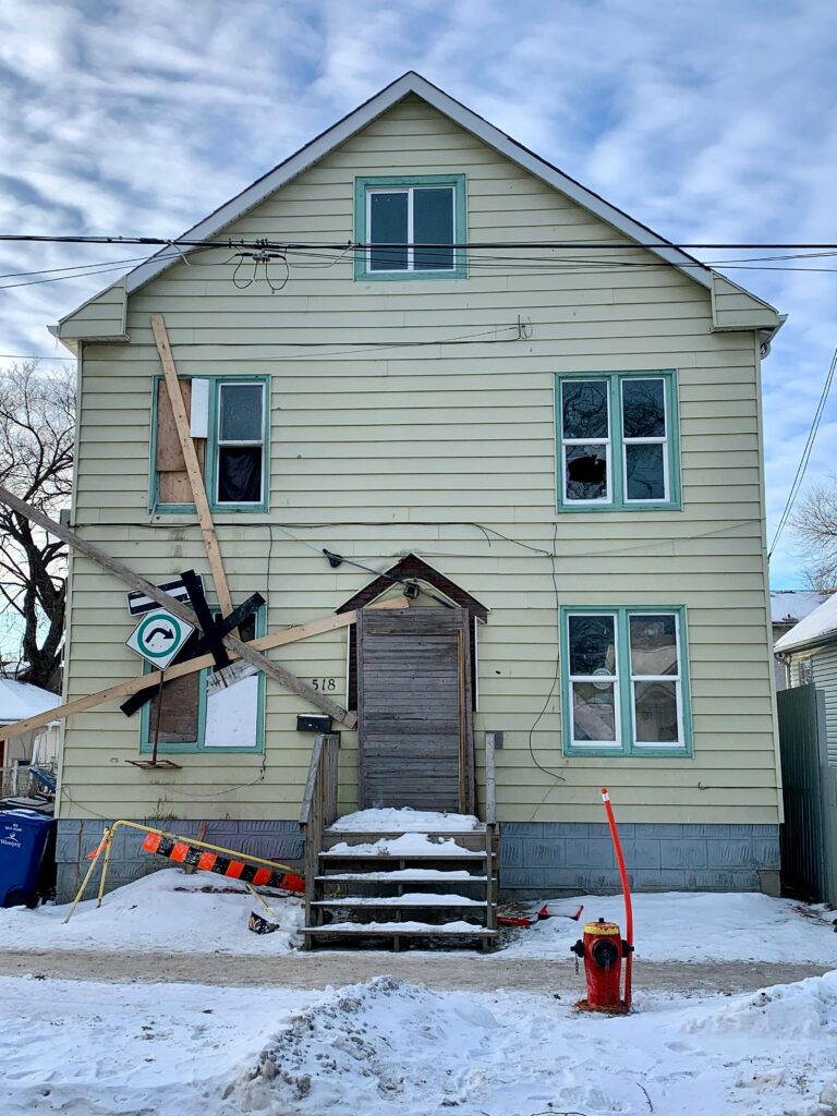 Boarded-up house in snowy Winnipeg, showing urban decay in winter.